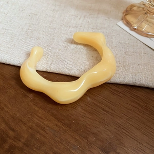 Detailed shot of yellow wavy acrylic open bracelet on a warm wooden and linen background
