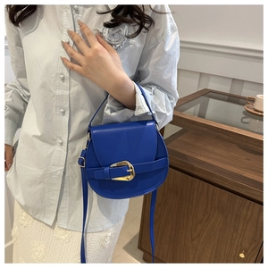 Close-up of a blue saddle crossbody bag with a large golden buckle and smooth finish