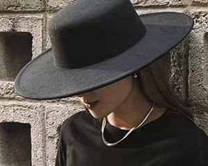 Close-up of black wide-brim wool felt hat with silver necklace in vintage outdoor lighting