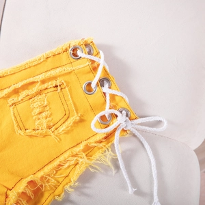 Dettaglio degli shorts di jeans gialli con occhielli in metallo e lacci bianchi laterali