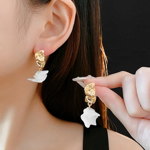 Détail d'une boucle d'oreille en métal doré avec pendentif en résine blanche à plusieurs niveaux