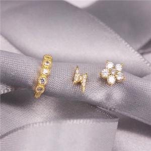 Macro shot of gold ear jewelry set with lightning bolt and flower studs on ribbon