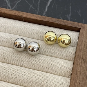 Detailed view of polished gold and silver ball stud earrings on a beige velvet jewelry tray