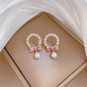 Macro view of gold bow earrings featuring pink heart zircon and elegant white pearls