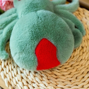 Close-up of green plush spider toy with detailed red hourglass marking on a woven mat