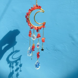 Macro detail of moon-shaped suncatcher with red crystals and prisms on blue wall