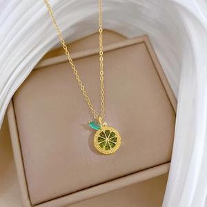 Detail of gold titanium necklace featuring a citrus lemon pendant with green gemstones