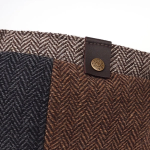 Macro shot of herringbone wool texture with leather trim and antique metal button detail