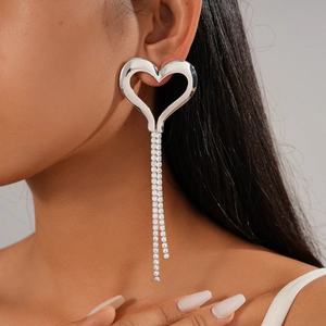 Close-up of silver hollow heart earrings with dangling zircon tassels on a model