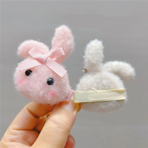 Close-up of pink and white plush bunny hair clips with bow details on a beige stand