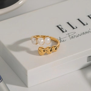 Detail of a gold open ring featuring three white pearls on a stylish white book