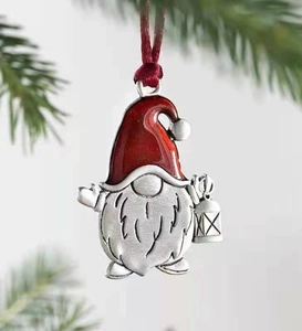 Detail of a red gnome Christmas ornament with a lantern on a green pine branch