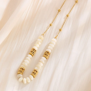 Detailed close-up of gold-plated titanium necklace with white beads on silk background