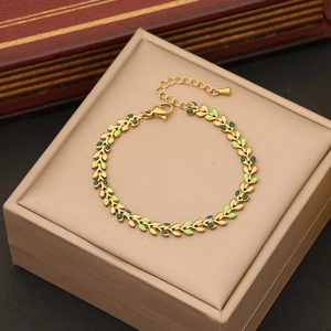 Golden wheat leaf bracelet with green enamel in a beige gift box on dark background