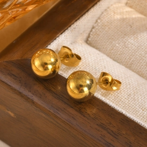 Detailed close-up of polished gold ball stud earrings resting in a premium wooden box