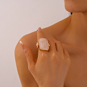 Detailed view of a rose quartz rectangle stone on a gold bezel set cocktail ring