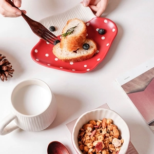 Flat lay of red strawberry ceramic plate with white mug and bowl set in a cozy scene