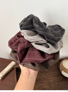 Detail of four striped fabric scrunchies in grey, burgundy and brown colors held in hand