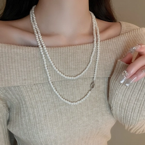 Nahaufnahme der eleganten doppelreihigen weißen Perlenkette auf beigem Strickpullover