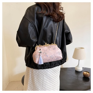 Detail view of a pink embroidered evening bag with a gold chain and tassel charm.
