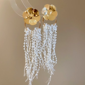 Detail of gold floral stud earrings with cascading white seed bead tassels on display