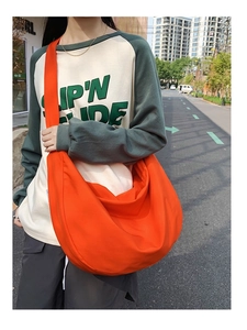 Close-up of a large orange oxford cloth crossbody bag worn by a model in a street setting