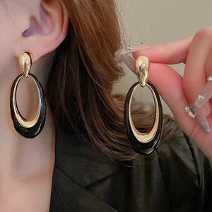 Macro detail of large geometric black lacquer and gold metal oval earrings on model