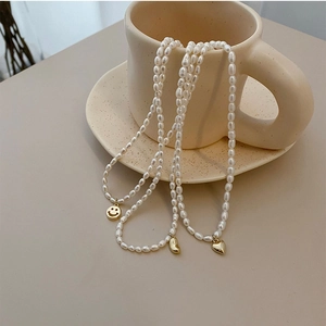 Three natural freshwater pearl necklaces with gold smiley, bean, and heart pendants on a cup