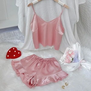Pink satin two-piece pajama set with V-neck camisole and ruffled shorts on white fur rug