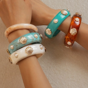 Détail de bracelets en résine avec breloques coquillages dorés et perles en couleurs variées