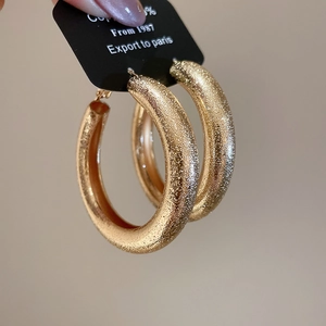 Close-up of golden thick hoop earrings with a textured glitter finish on black card