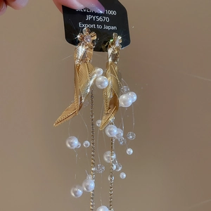 Detail of elegant gold leaf earrings with hanging white pearls and long fluid tassels