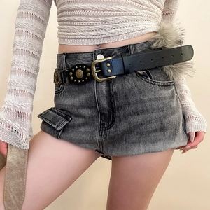 Détail d'une ceinture en cuir noir avec clous dorés et boucle vintage sur short en jean