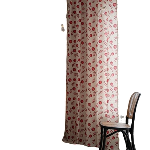 Red Christmas ball patterned semi-sheer beige curtain hanging next to a rattan chair
