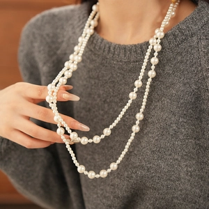 Detail view of multi-layer pearl necklace layered on grey sweater for elegant winter style