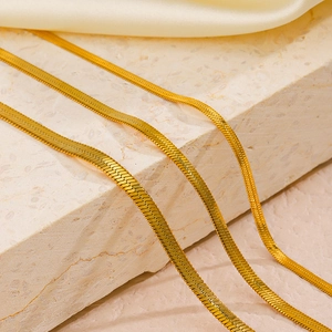 Golden stainless steel flat snake bone bracelets in three widths on marble and silk background
