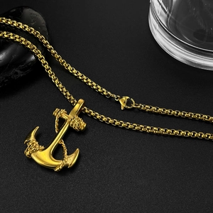 Detailed close-up of golden anchor cross pendant with matching box chain on dark stones