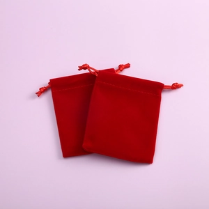 Close-up of two red velvet drawstring jewelry pouches on a soft purple background