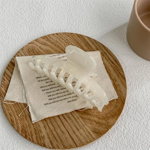 Macro detail of large translucent white acetate hair claw clip on aesthetic linen background