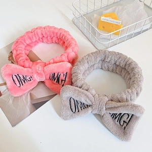 Pink and gray plush spa headbands with OMG embroidery and bow detail shown on a tray