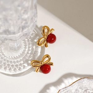 Détail de boucles d'oreilles nœud vintage avec finition dorée et perles rouges sur porcelaine