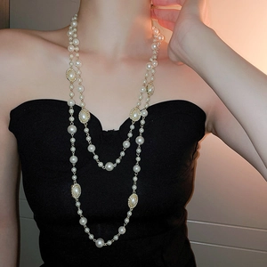Detail of layered white pearl necklace with gold charms on black dress background