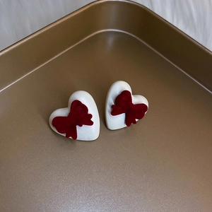 Detail of red flocked bow on white heart stud earring in vintage bronze tray