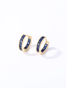 Detalle de pendientes de aro dorados con circonita azul cuadrada y acabado pulido