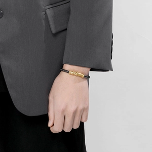Detail of black braided leather bracelet with gold cylindrical charm on male wrist