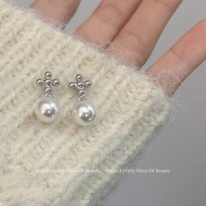 Boucles d'oreilles croix en argent avec perles rondes sur un fond en maille douce