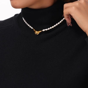 Elegant pearl necklace with a golden hand clasp worn over a black sweater