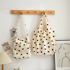 Set of textured canvas bags with black heart prints hanging on a light wooden rack