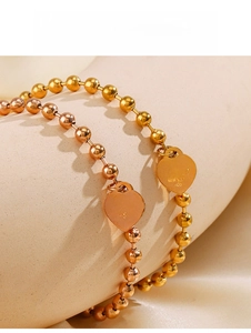 Macro shot of gold and rose gold beaded bracelets with engraved heart charm pendants
