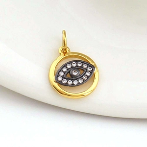Evil eye pendant with 18k gold plating and white crystals on a white ceramic background